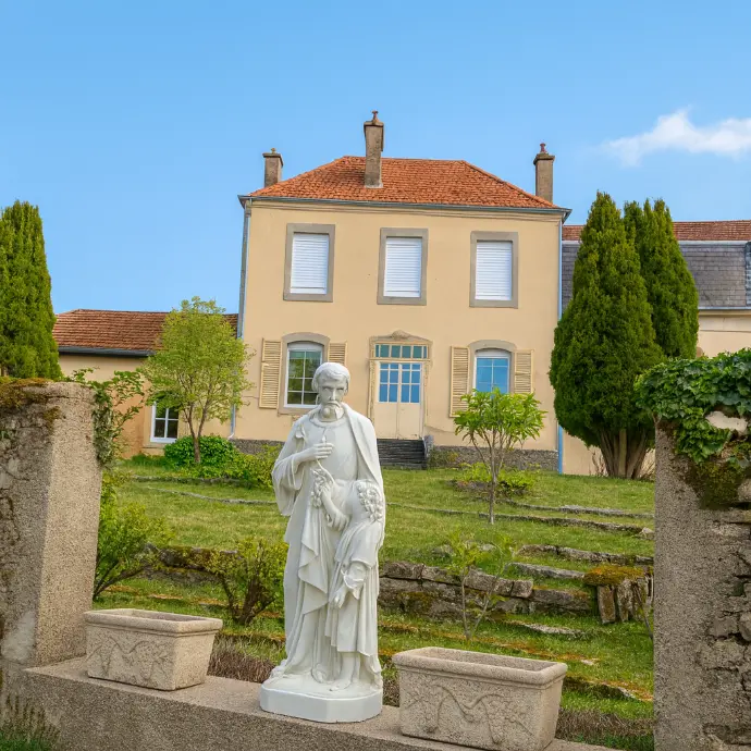 façade rénovée d’un bâtiment du domaine avec statue blanche religieuse au premier plan dans le jardin