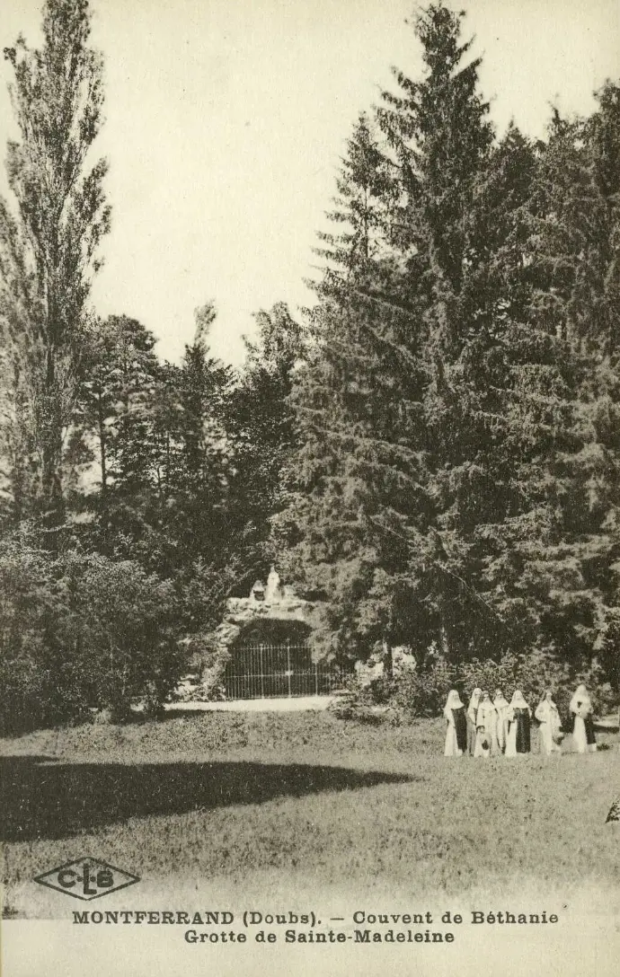 ancienne photographie d’archive de la grotte Sainte-Madeleine, une chapelle naturelle dans le parc du Couvent de Béthanie, avec un groupe de sœurs rassemblées, entourées de grands arbres