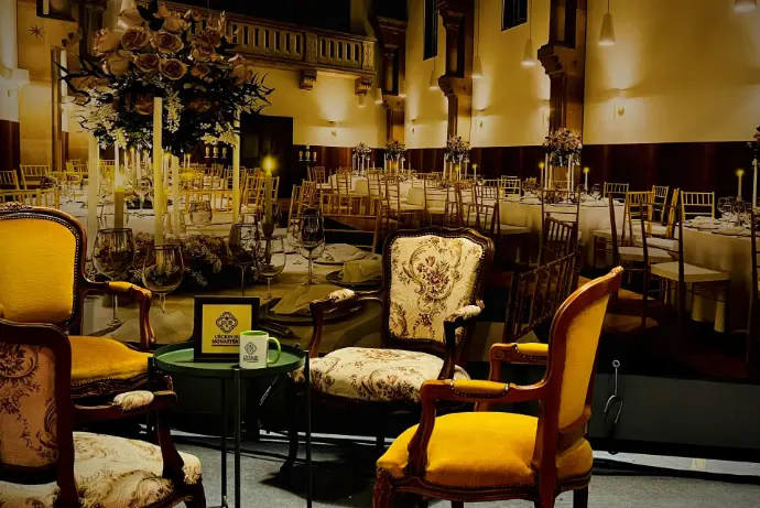 Gros plan sur le stand de L’Écrin du Monastère au Salon des Mariés de Besançon, avec fauteuils anciens autour d’une petite table et en fond un visuel de salle de réception dressée.