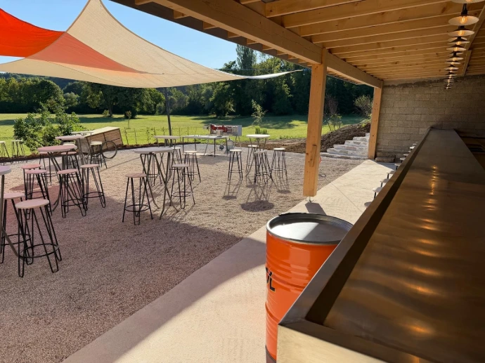 Bar extérieur couvert avec comptoir, tables hautes et vue sur le parc de L’Écrin du Monastère, dans le Doubs.