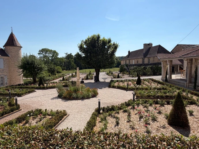 Roseraie en journée avec allées paysagées, massifs fleuris et vue sur les bâtiments de L’Écrin du Monastère, à Montferrand-le-Château.